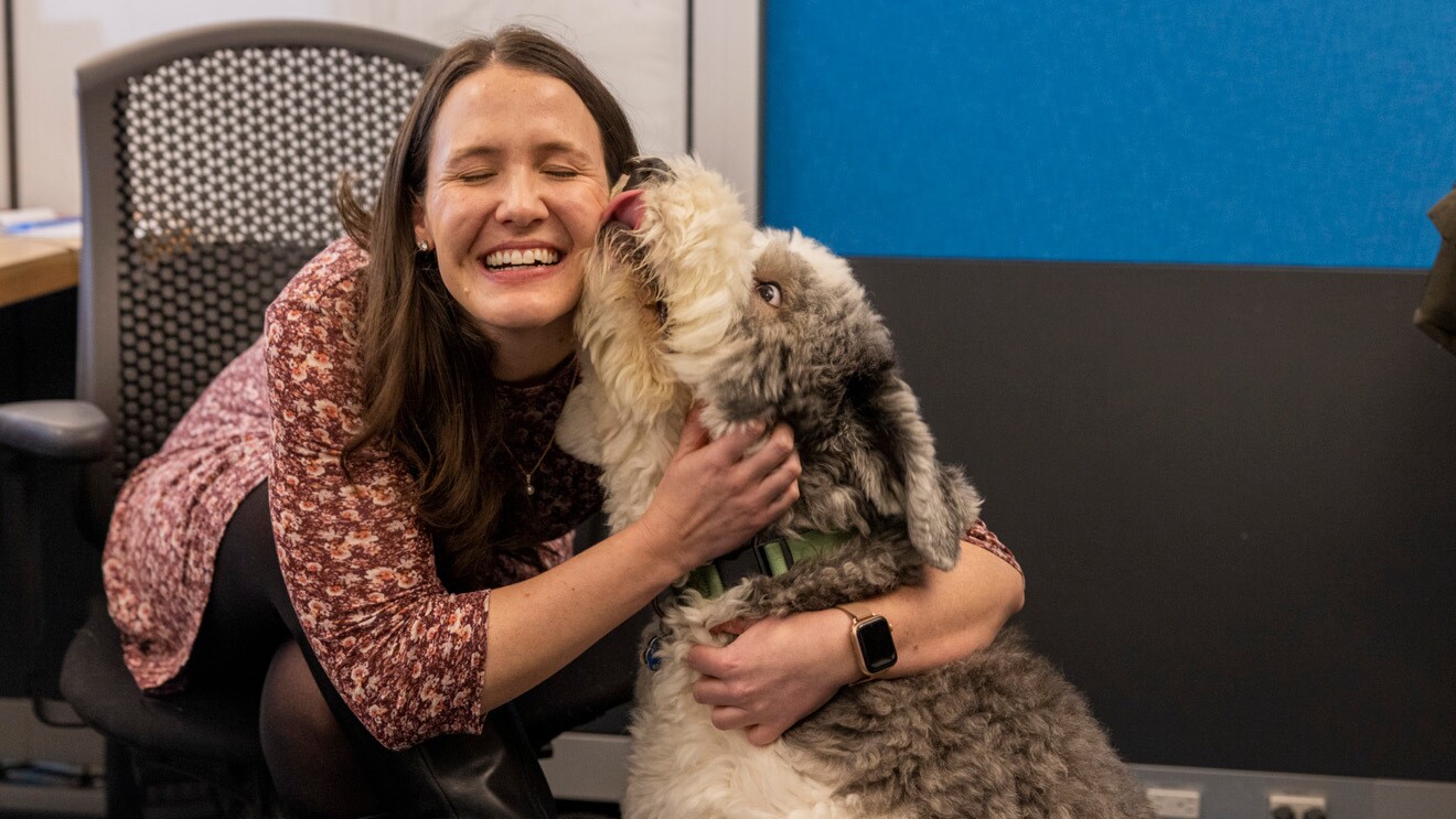 An Amazon employee smiles while her dog licks her cheek.