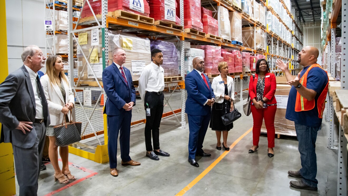 An image of Abe Diaz speaking to a group of people in an aisle of an Amazon fulfillment center where Amazon has its disaster relief hub.