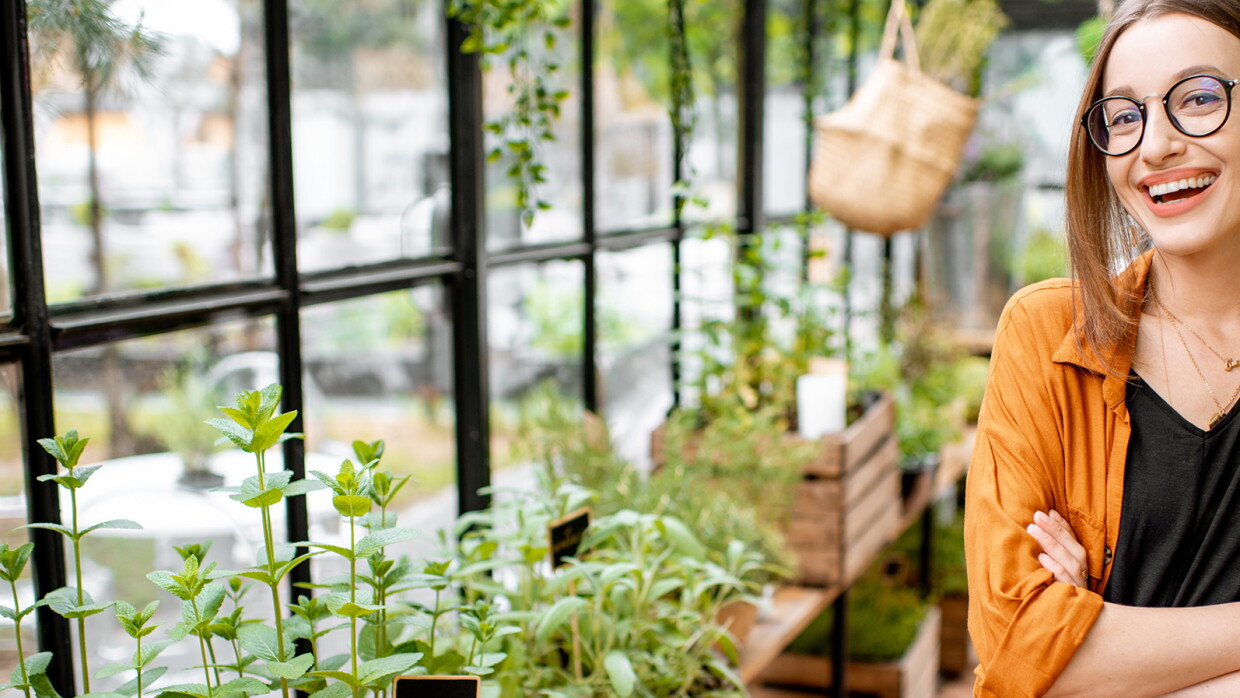 A woman smiles from inside a green house, her arms crossed.