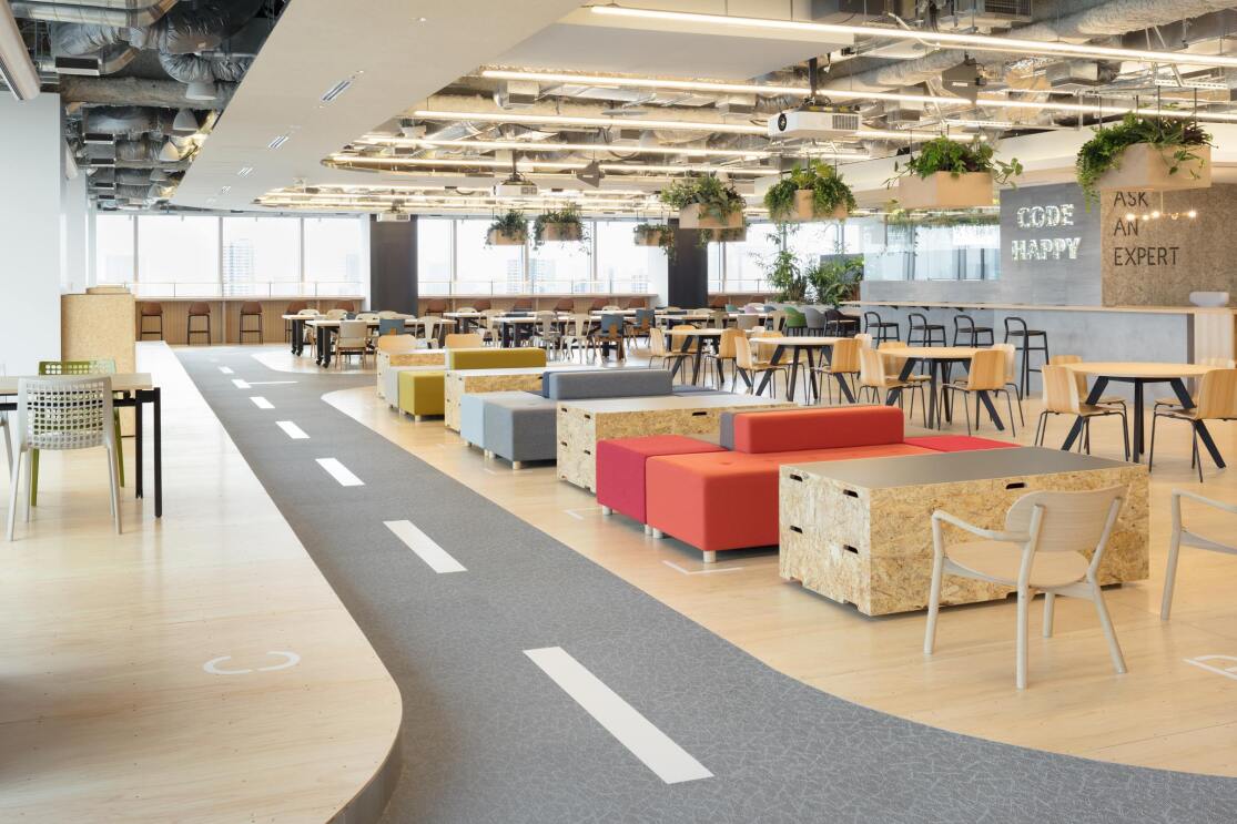 道路のようなセンターラインがある通路の横にテーブルなどが置かれている広いスペース。天井から植物が入ったかごが吊るされている