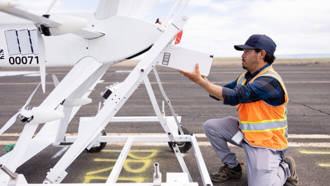 Images of Amazon employees wearing orange safety vests work on drones.