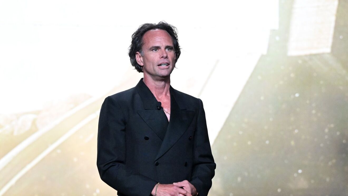 Man in black suit jacket on stage with dramatic lighting.
