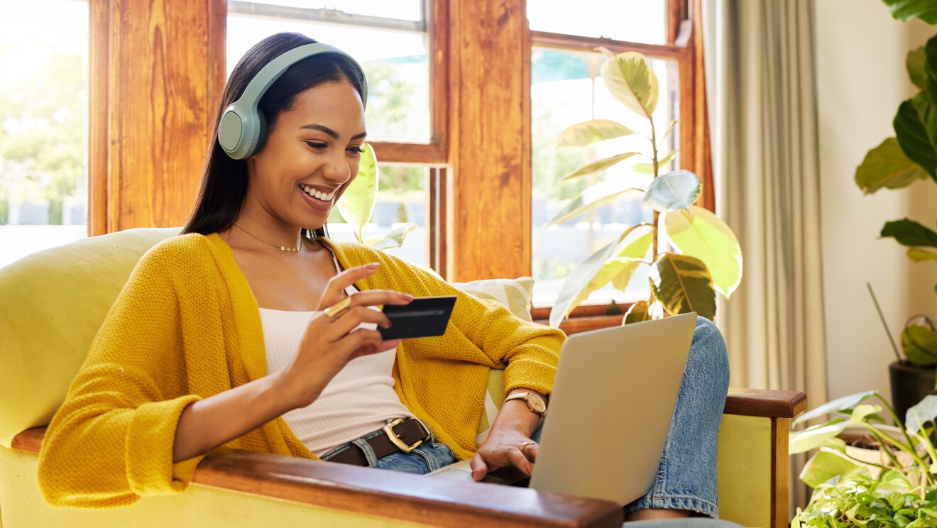 A girl in yellow outer is smiling while looking at her computer and holding a card