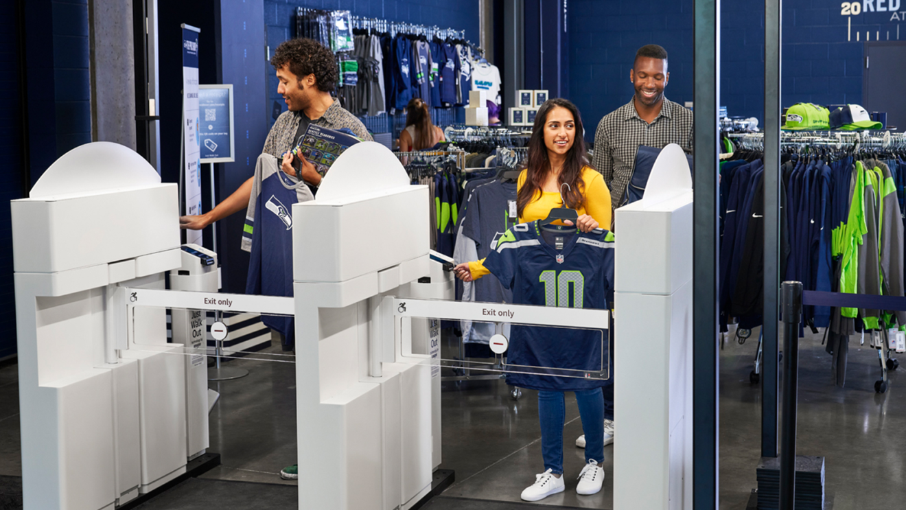 A photo of three customers purchasing Seahawks merchandise with Just Walk Out Technology at a retail store in Lumen Field.