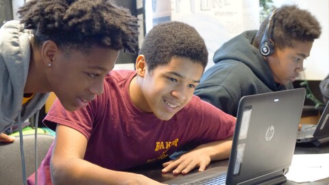 Students use a laptop in a classroom while working together on a coding project.