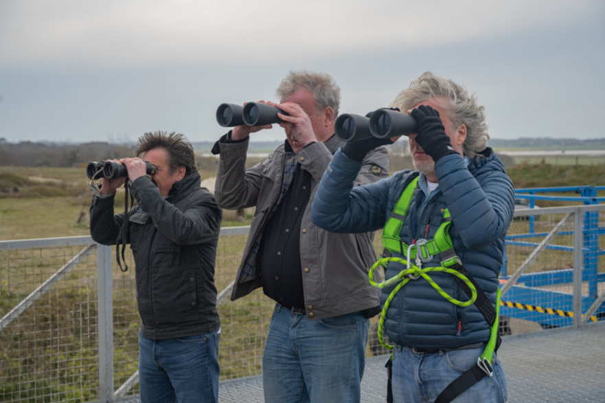 Three men holding binoculars while standing in a field