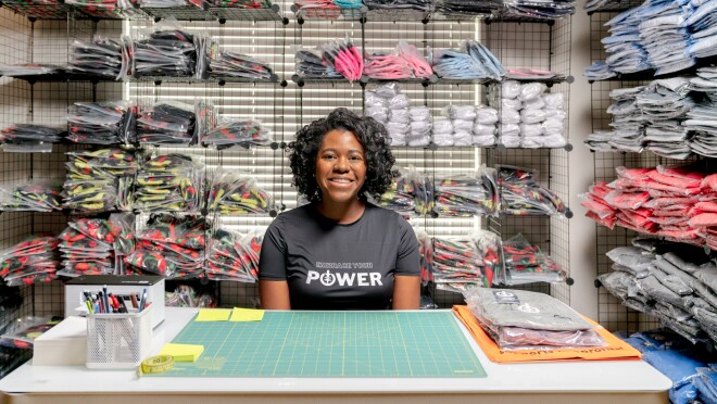 安吉尔·约翰逊(Angel Johnson)坐在办公桌前,微笑着被包装好的ICONI服装包围着。