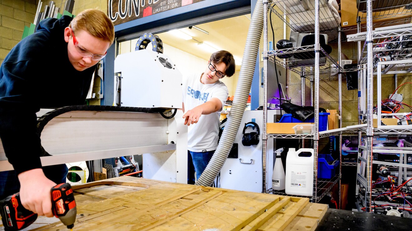 A photo of a student drilling a piece of wood in a high school robotics shop.