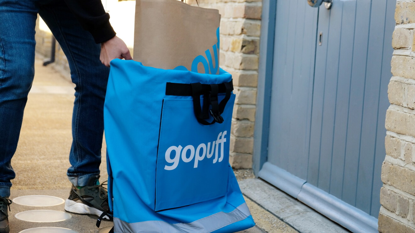 Delivery person holding Gopuff bag and paper shopping bag at doorstep

