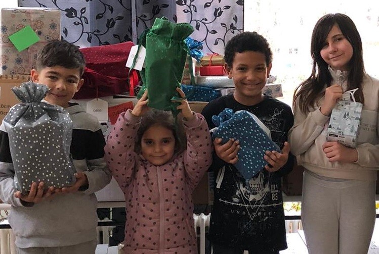 Kinder zeigen stolz ihre Geschenke. Ein kleines Mädchen hält ein grünes Präsent hoch über seinen Kopf.