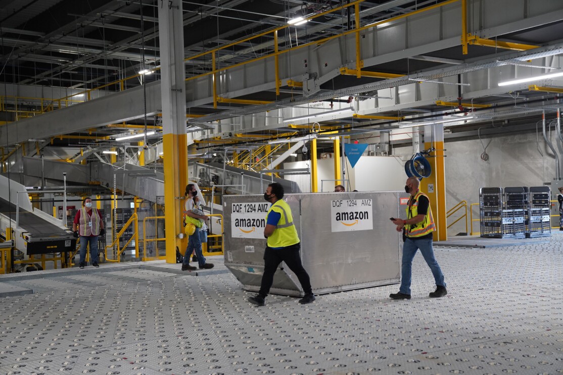 An image of a large metal container in the middle of an Amazon sortation center. There are employees in safety vests walking around the container.