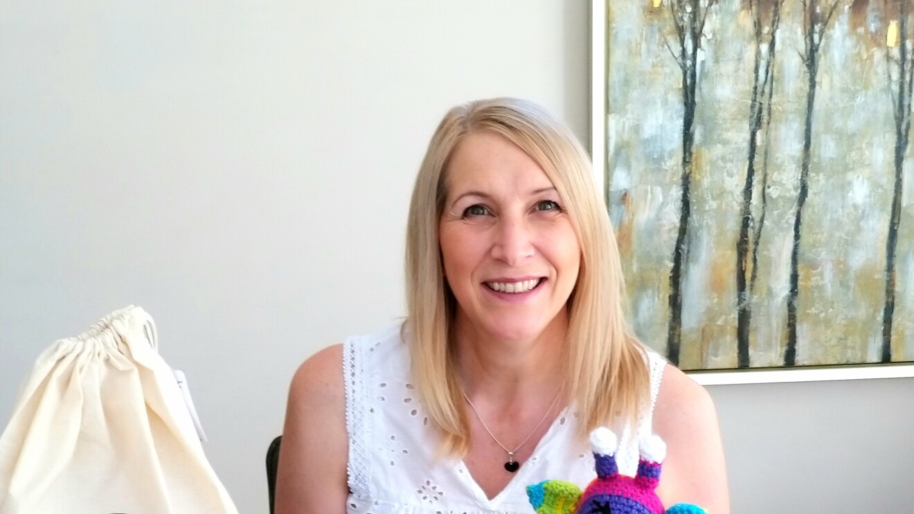 Lisa Dobbs from Wee Woolly Wonderfuls sitting behind some of the toys that she has made using her crochet kits.