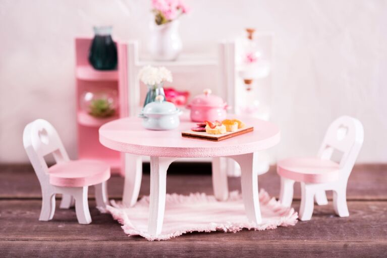 ピンク色のミニチュアティーセット、ミニテーブルとイス、ミニラグなどが置かれている