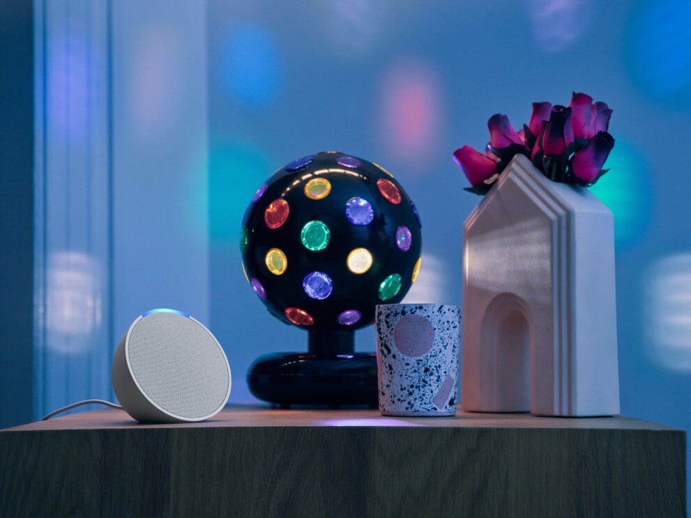 Amazon Echo Pop sits on table next to disco ball and vase with flowers