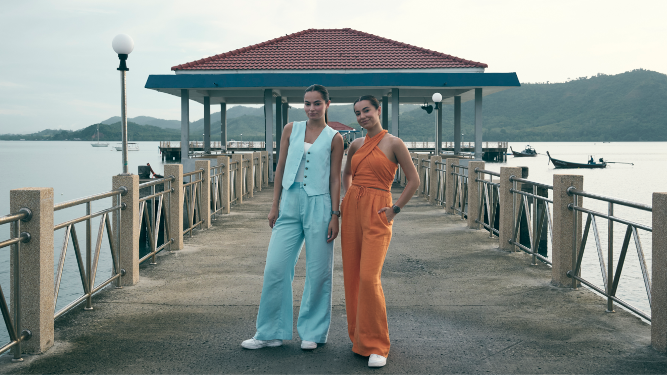 Two young women looking into camera while stood on a pier