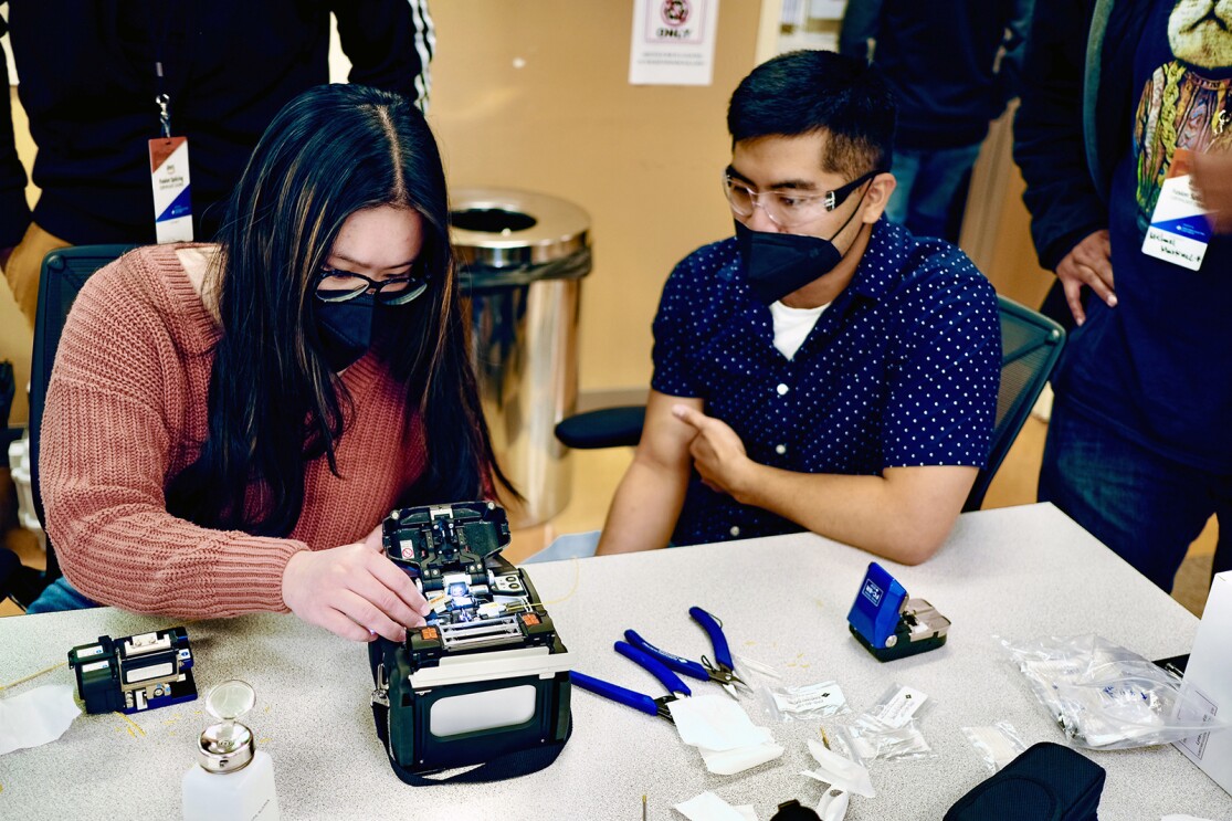 An image of two people working on a piece of technology hardware in a class setting. 