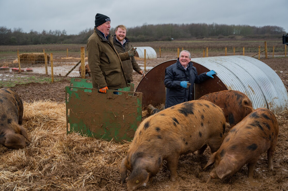 Jeremy Clarkson standing near Kaleb Cooper and pigs on his 1,000-acre farm (Diddly Squat Farm) in the Cotswolds.