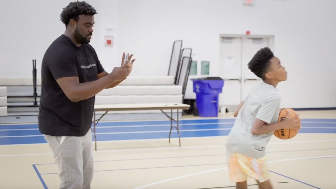 A photo of a customer taking a photo of a child playing basketball on their phone.