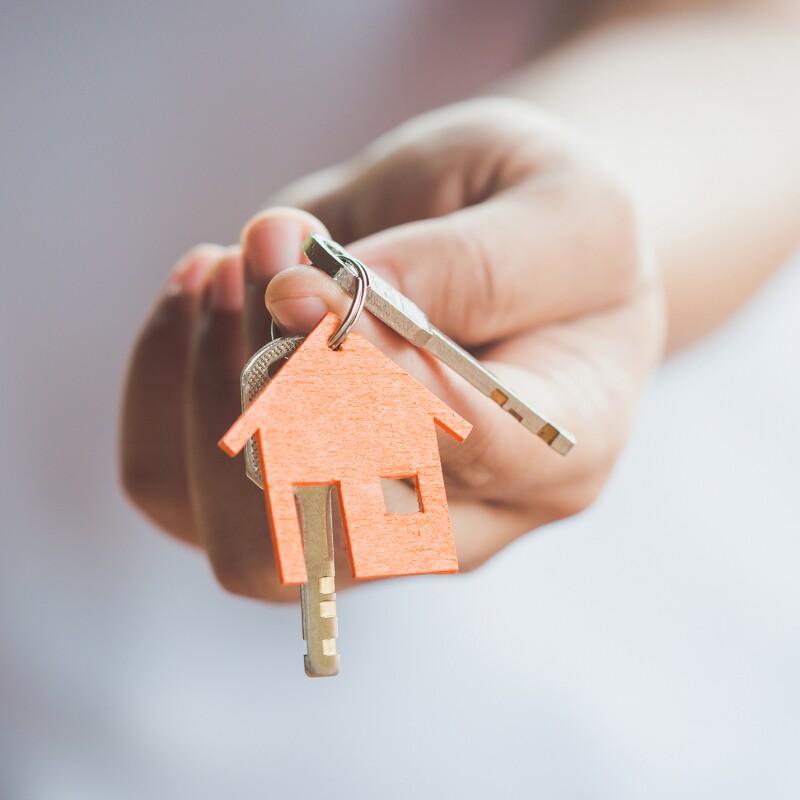 A woman's hand holding a set of keys with a keychain that shows a house on it.