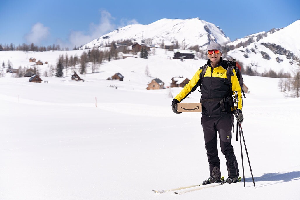 Helmut Edelmaier wears his ski gear and holds an Amazon package at the mountan village.