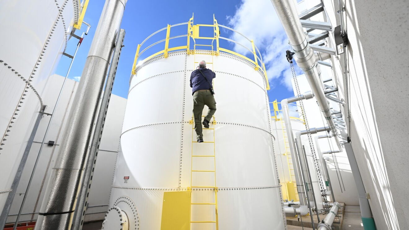A person climbs up a water tower via a yellow ladder connected to the tower.