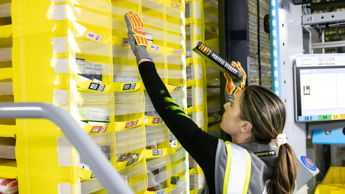 Warehouse worker reaching up to insert an item in to yellow storage shelves