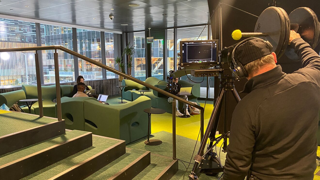 An image of a film crew filming a group of people sitting in the lobby of an Amazon office building on their laptops.