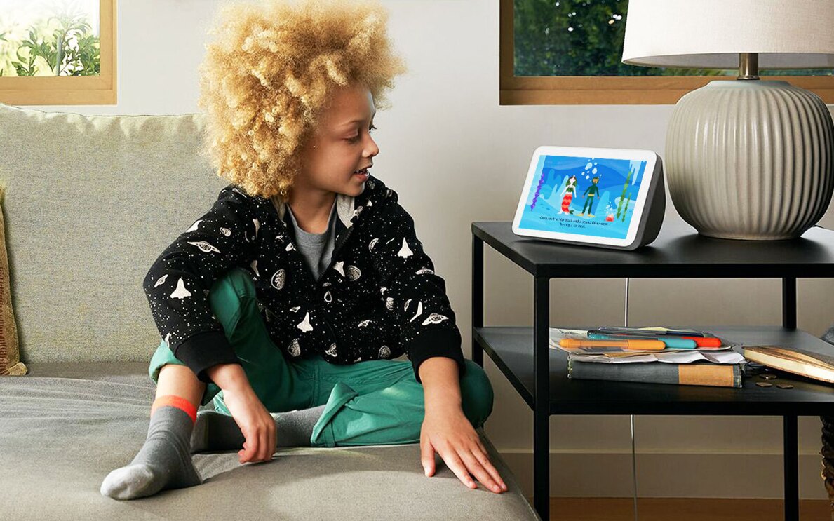 A child sits on a chair in a living room and looks at an Amazon Echo with Create with Alexa displayed on the screen.