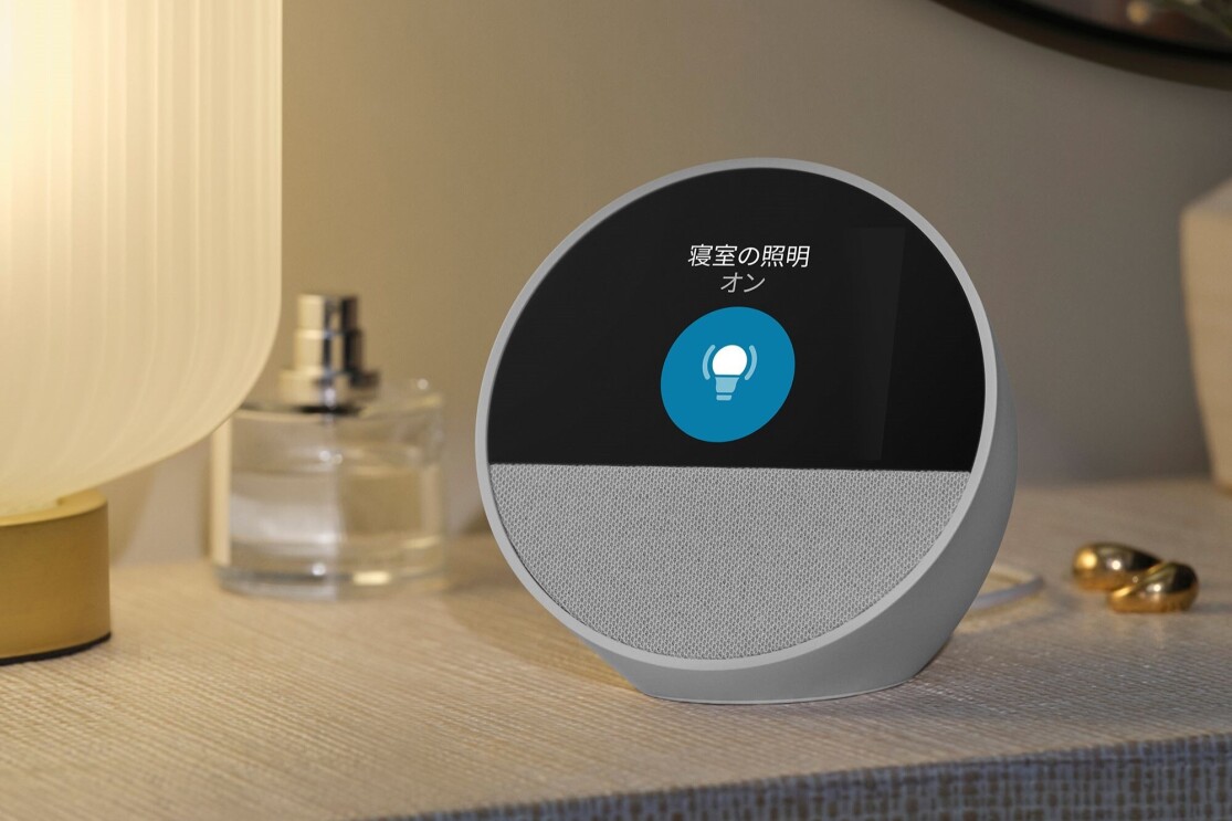 白いデジタル時計(Echo Spot)が照明と香水、イヤリングなどと一緒にテーブルに置かれている。Echi Spotの画面には「寝室の照明オン」という文字と円形にランプのマークが表示されている