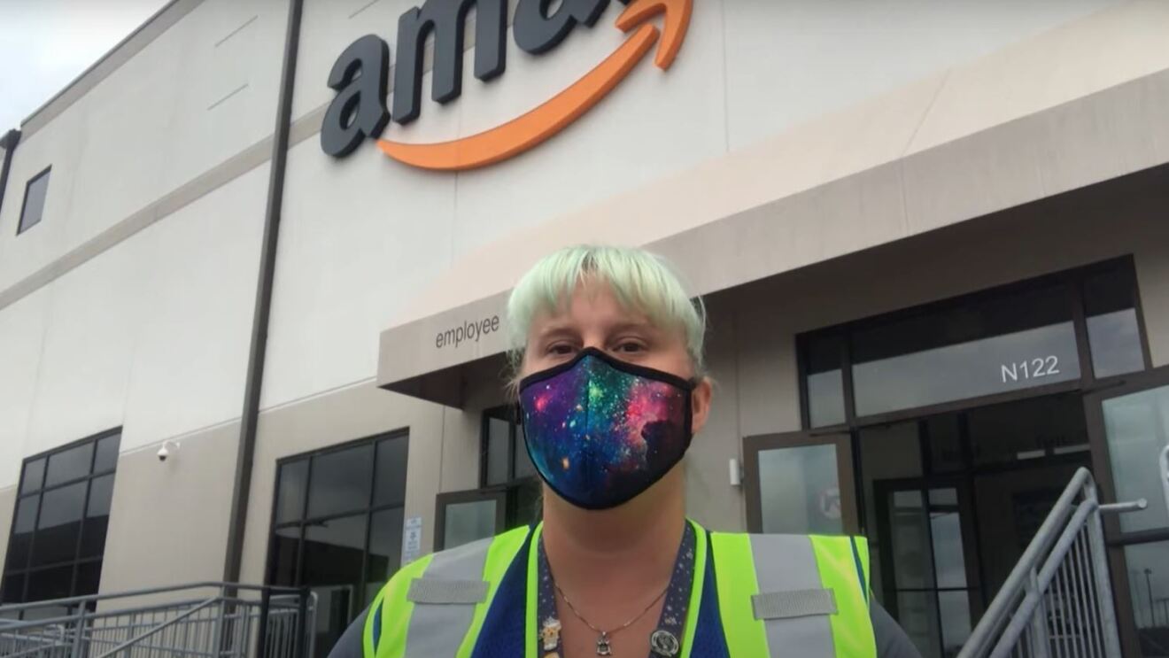 A woman wearing a mask and a safety vest stands in front of an Amazon fulfillment center