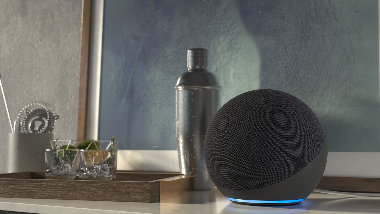 An image of an Echo device sitting on a side table next to a framed artwork and other home decor.