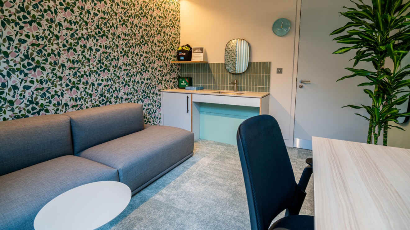 Modern office lounge with floral wallpaper and grey sofa