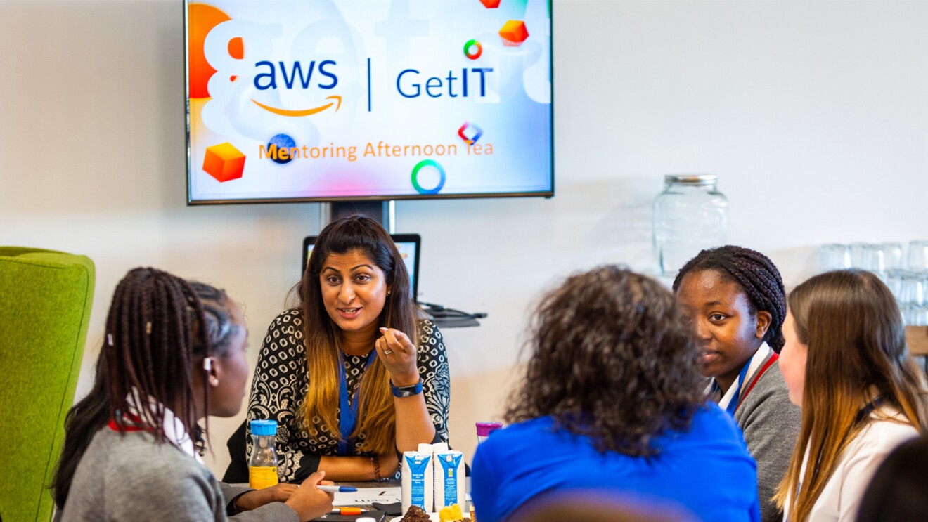 An image of five women working together in a meeting room at an AWS office.