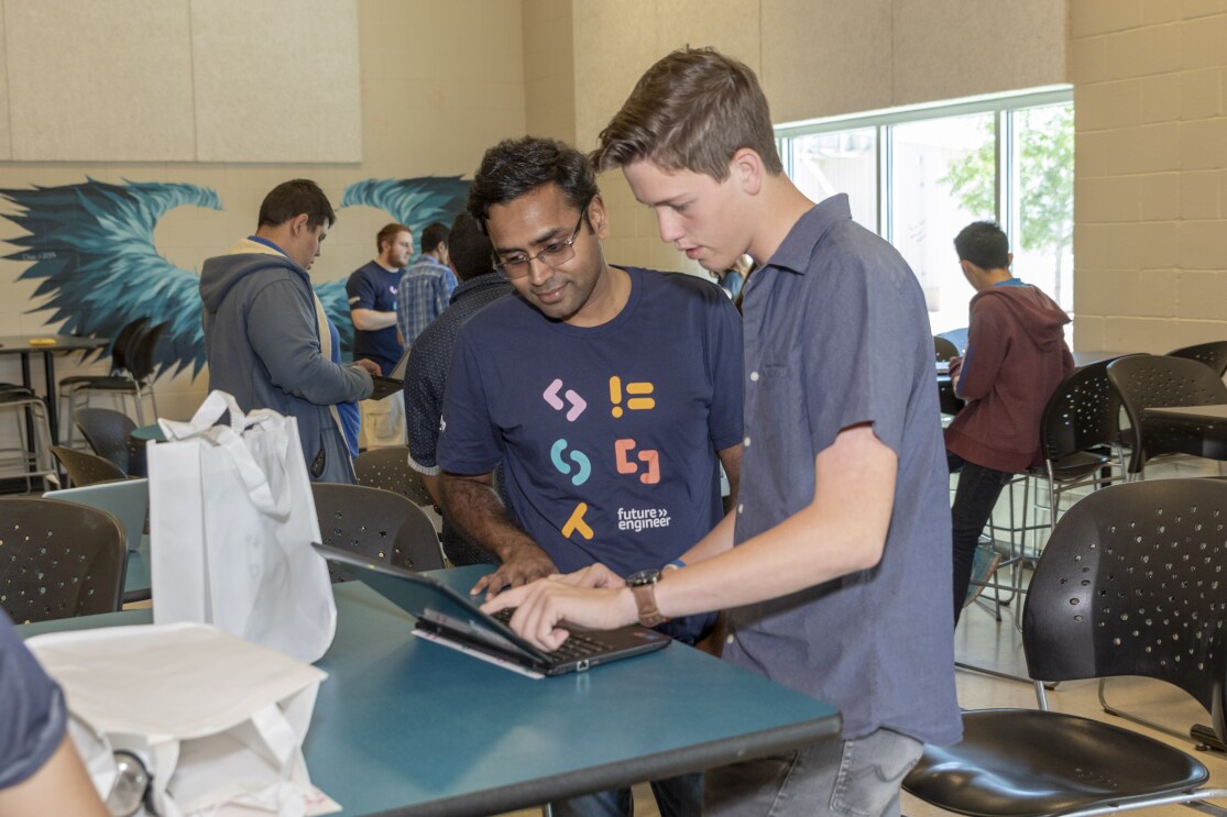 A student works on a computer, while discussing what's on his screen with an Amazonian.