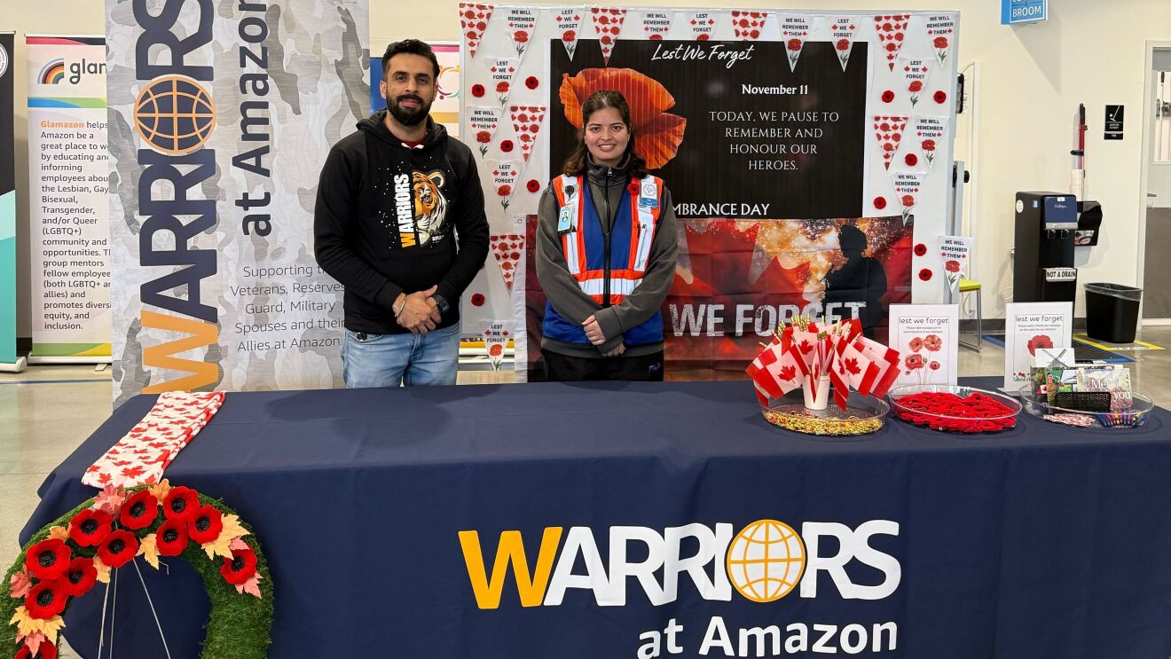 Two Amazon employees standing at a Warriors at Amazon desk surrounded by poppies and Canadian flags