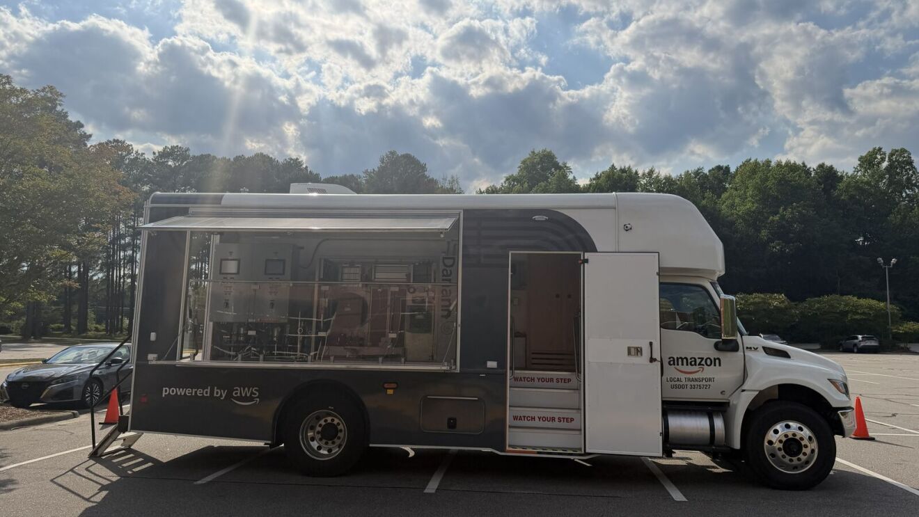AWS and Amazon branded truck with transparent side revealing automated warehouse technology inside