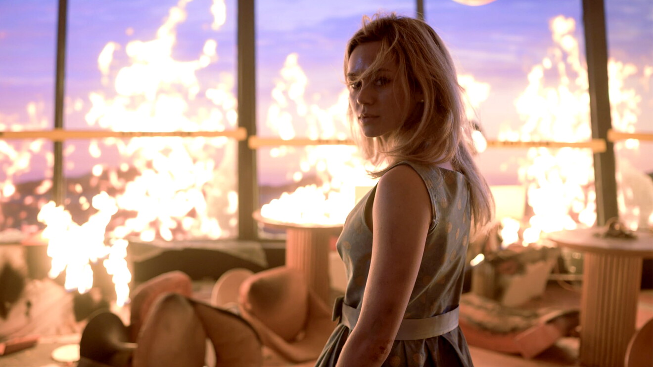 Woman in sleeveless dress standing amid flames engulfing room