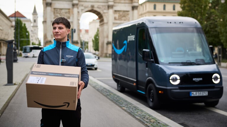 Amazon Fahrer mit einem Paket, im Hintergrund ein Rivian Elektrolieferfahrzeug
