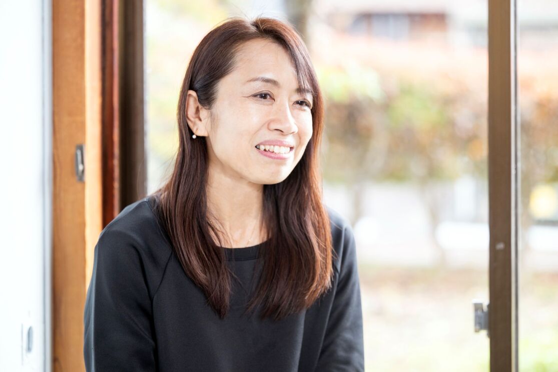 黒いTシャツを着ている女性が話している。彼女は窓の近くに座っている。