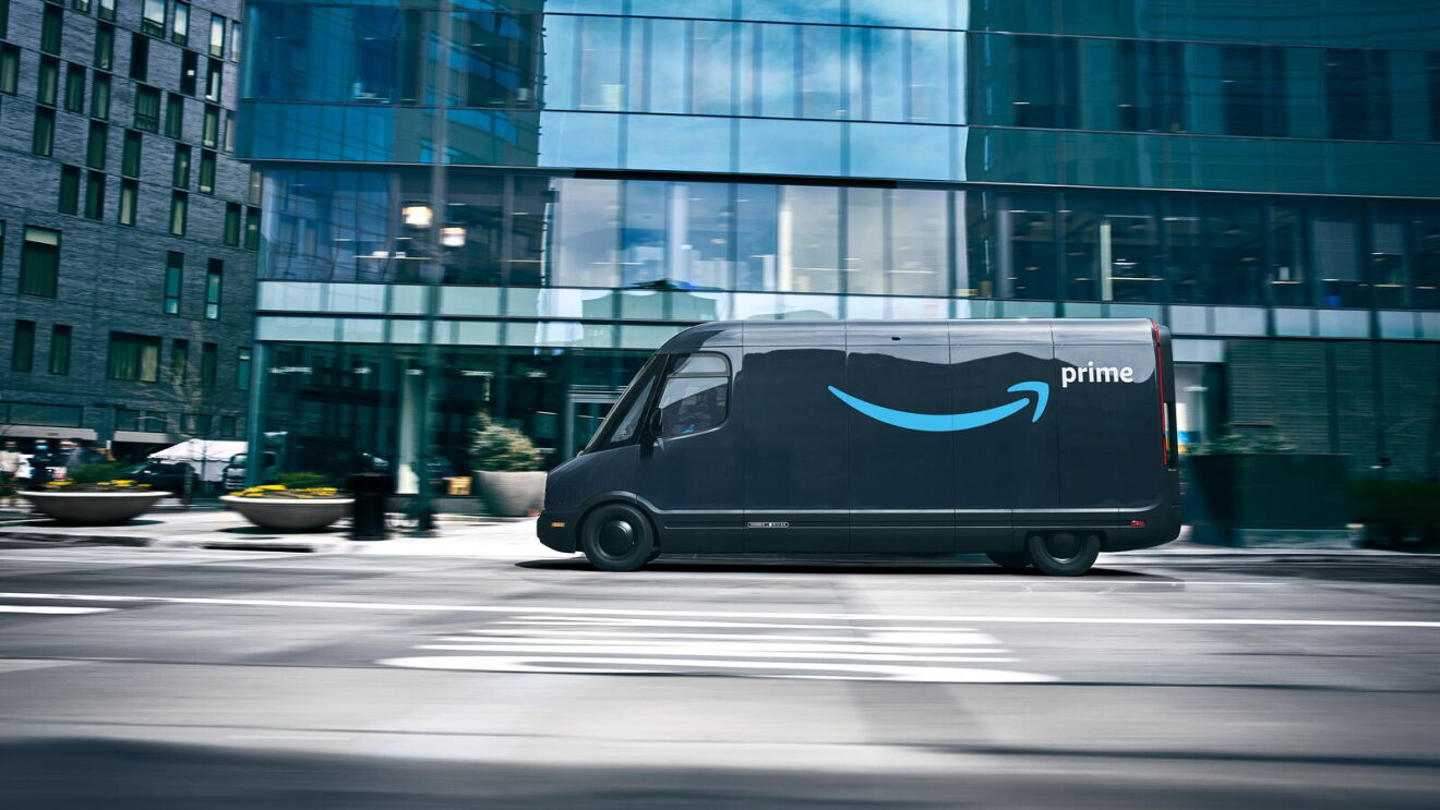 Amazon Rivian delivery van driving on city street past modern glass buildings