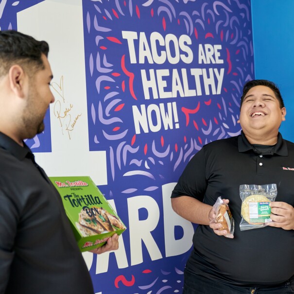 Ronald and Anthony  hold their products in front of a Mr. Tortilla promotional sign.