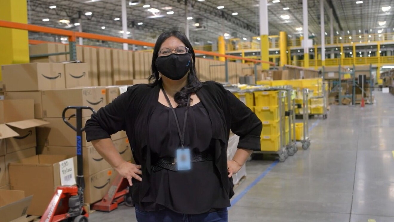 An Amazon employee stands with her hands on her hips as she poses for a picture in a fulfillment center.