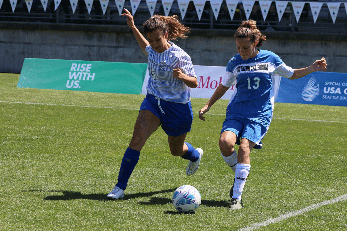 An image of two soccer players running to kick a ball in a soccer field during the Special Olympics. The person on the right is wearing a shirt that says "Southern California."