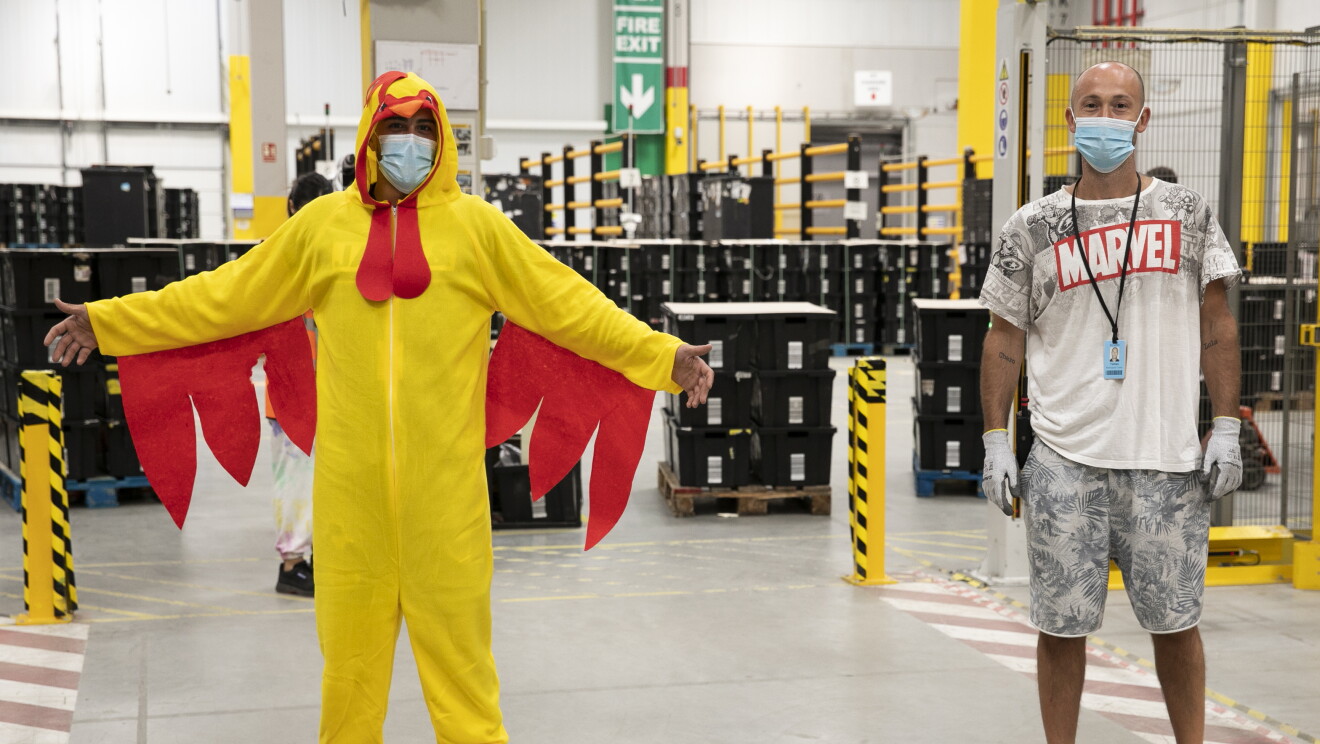 PJammin en MAD6 Illescas. Dentro del centro logístico con las cajas negrad detrás hay dos asociados vestidos en pijama. El de la izquierda va de gallo y el de la derecha con un pijama de manga y pantalón corto de Marvel. 
