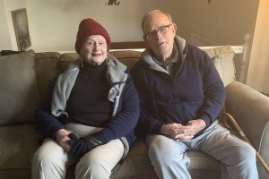 An image of a man and a woman sitting on a couch in their home, smiling for a photo.