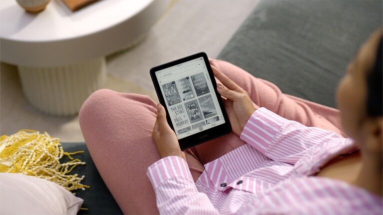 Hands holding Kindle displaying book covers in cozy home setting