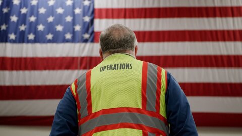 一张克林特·卡罗尔看着面前一面巨大的美国国旗的照片。这张照片是从克林特身后拍摄的,你可以看到他的黄色背心上写着“手术”。