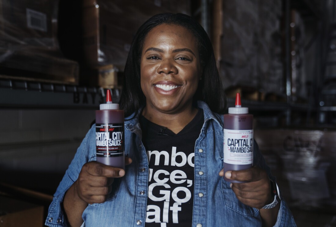 Arsha Jones holds up the two different flavors of sauces she makes and smiles for the camera.