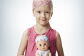 Una niña de unos diez años con un pañuelo en la cabeza sujetando una muñeca también con pañuelo. La niña luce un jersey rosa sin mangas. 