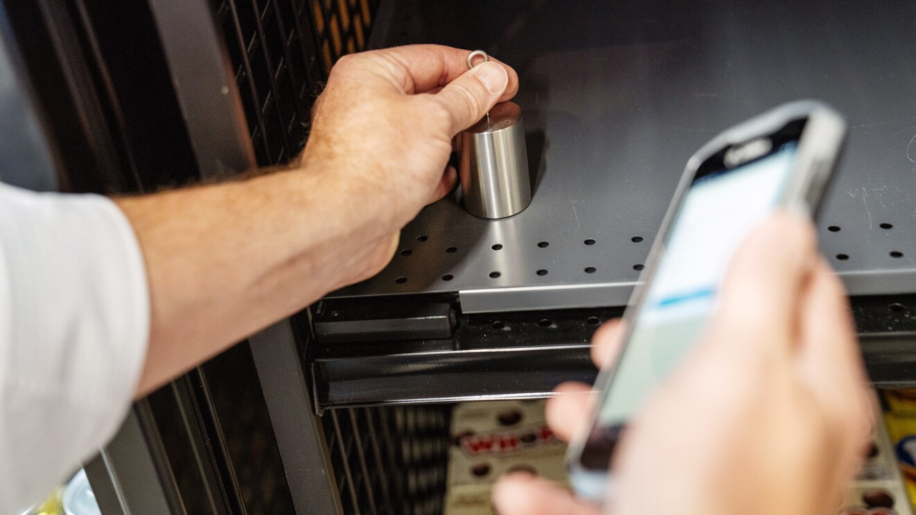 Just Walk Out Technology: hand places a weight used to calibrate shelf sensors on a shelf in Amazon's Just Walk Out lab